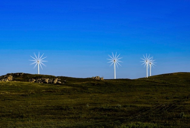 A wind farm and a solar panel array side-by-side in a rural landscape, with rolling hills and a clear blue sky in the background. This visually showcases renewable energy sources.